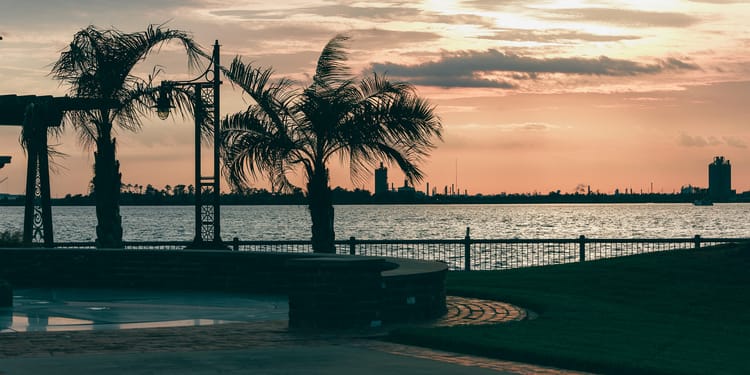 Lake Charles Louisiana waterfront at sunset with palm trees and industrial skyline