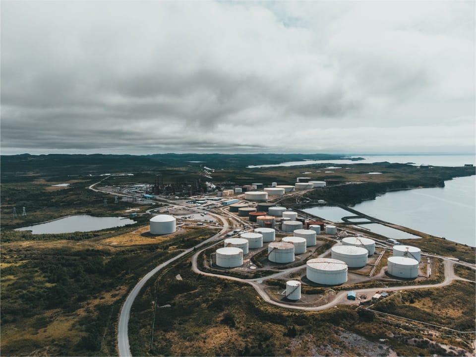 Aerial view of coastal oil storage tanks and refinery infrastructure beside a body of water.